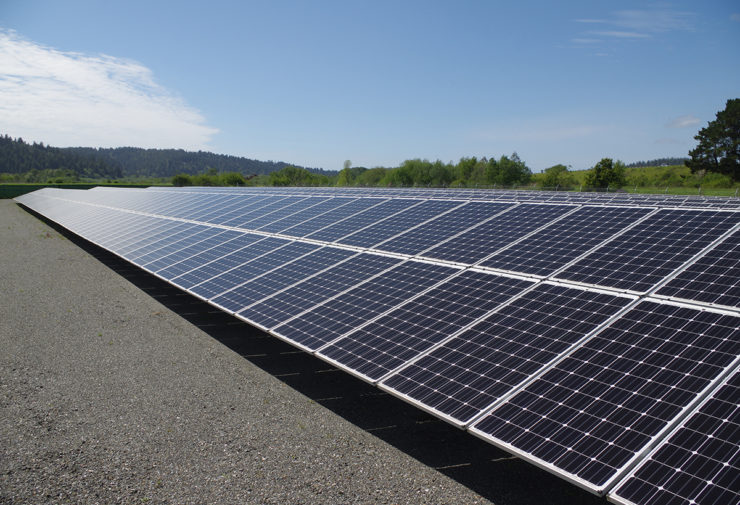 The array reflects sun, with low hills and blue sky beyond.