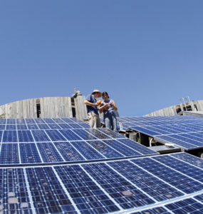 Two students discuss testing equipment while standing amidst the Trinidad array modules.