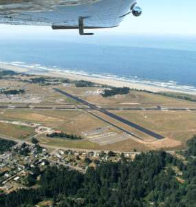 The aiport landing strips and ocean are shown beneath a plane's wing.