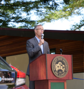 Jared Huffman speaks from a podium, between a zero-emission vehicle and the West Wing