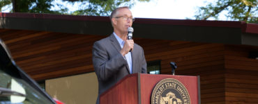 Jared Huffman speaks from a podium, between a zero-emission vehicle and the West Wing