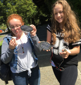 Two middle school students hold solar modules and fans in the sun.