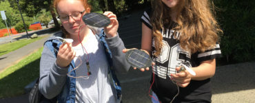 Two middle school students hold solar modules and fans in the sun.