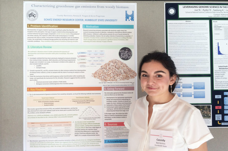 Cassidy Barrientos stands in front of the project poster, wearing a white blouse and a nametag