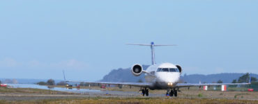 A plane moves along the runway, with Trinidad, CA in the distance