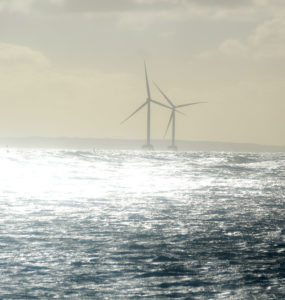 Light shines brightly over two offshore wind turbines and the ocean