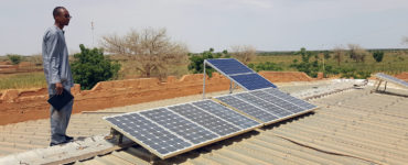 A clinic worker stands on the roof beside a small solar array