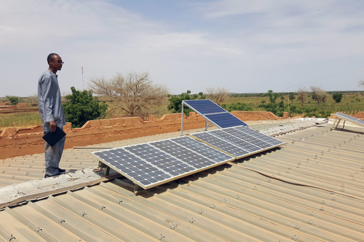 A clinic worker stands on the roof beside a small solar array