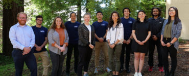 11 students stand together beneath redwoods