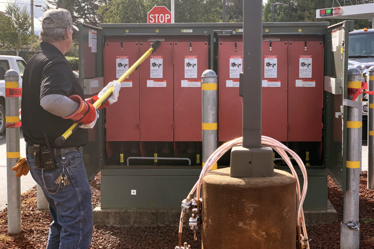 An electrician removes fuse covers using a safety pole