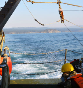 Two researchers sit near the stern with the shore receding in the distance