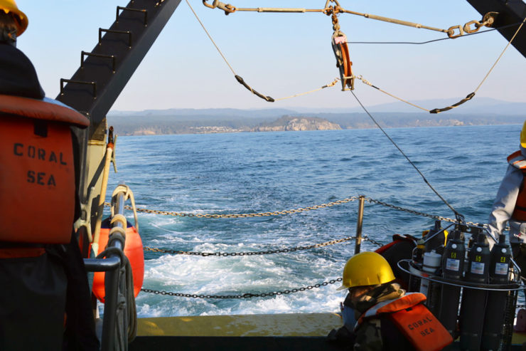 Two researchers sit near the stern with the shore receding in the distance