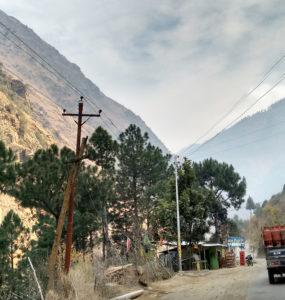 A truck drives past a small roadway shop in the mountains, with power lines overhead.