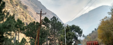 A truck drives past a small roadway shop in the mountains, with power lines overhead.