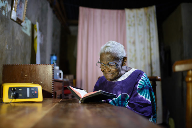A elder woman reads at a dining room table by solar light