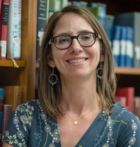 A woman stands smiling in front of a bookcase