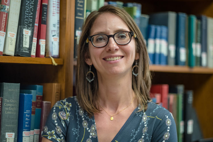 A woman stands smiling in front of a bookcase