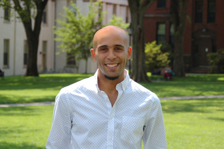 A smiling man in a white shirt stands on a grassy lawn