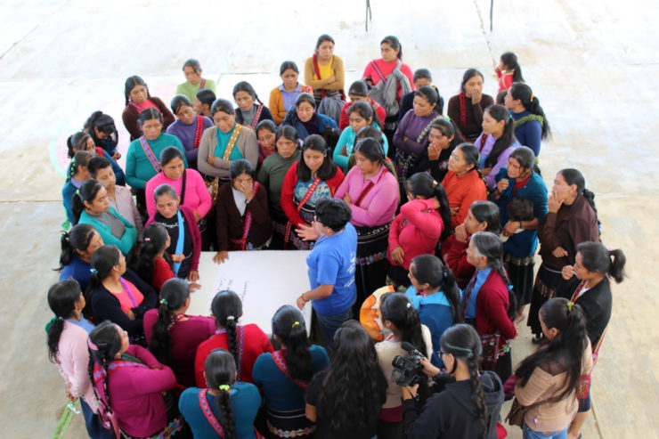 Over 50 women gather in a close circle to listen to a speaker