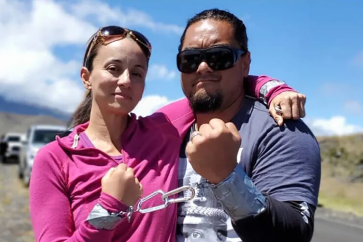 Two people stand with one arm around each other's shoulder and the other wrists locked together