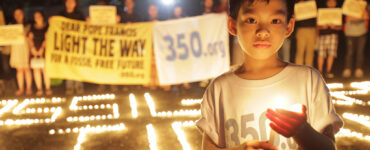 A child is holding a candle and wearing a shirt that says "350.org"