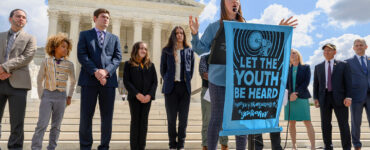 A young person speaks outside a courthouse, behind a banner that says "Let the youth be heard."