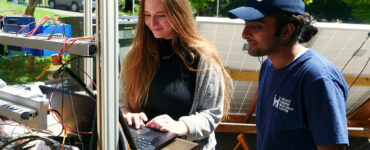Students stand at a computer, operating a solar water pump